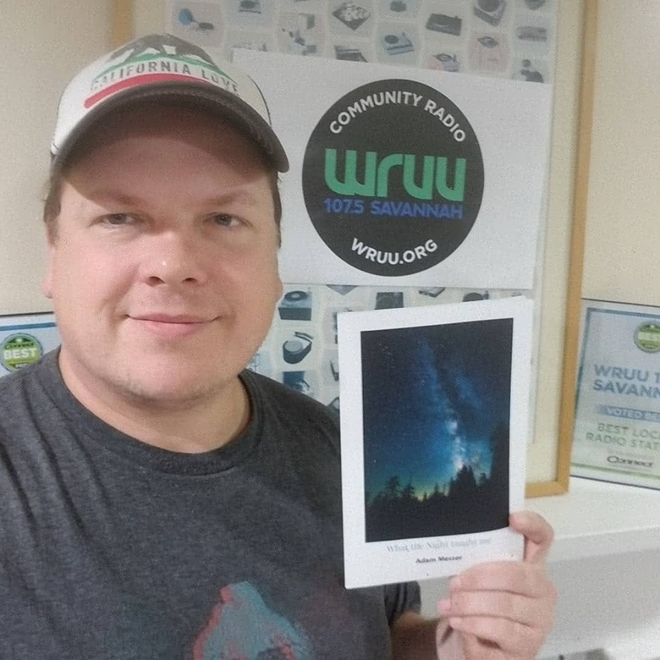 Adam Messer holding up his poetry book What the night taught me. Background is at the WRUU 107.5 FM Savannah studio.